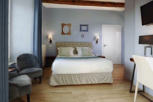 A bedroom with a large bed, two bedside tables, a chair, a TV, and a door. - Hôtel Joyet de Maubec (Uzerche)
