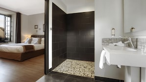 A modern hotel room with a large bed, a separate shower area, and a bathroom with a white sink and mirror. - Hôtel Joyet de Maubec (Uzerche)