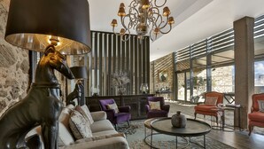 A spacious lobby with a modern chandelier, leather sofas, and a stone wall. - Hôtel Joyet de Maubec (Uzerche)