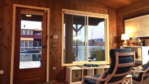 A wooden interior with a large window, two blue-striped lounge chairs, a small table, and a map on the wall.
