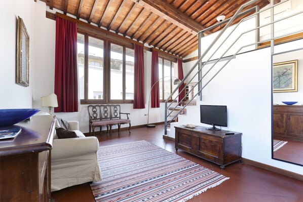 Uma sala de estar ampla com teto alto, escada, televisão e uma grande janela com cortinas.