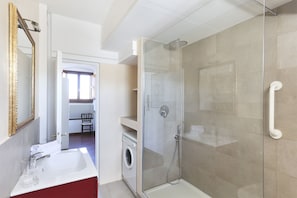 Uma casa de banho moderna com cabine de duche em vidro, lavatório branco com armário vermelho e máquina de lavar roupa.