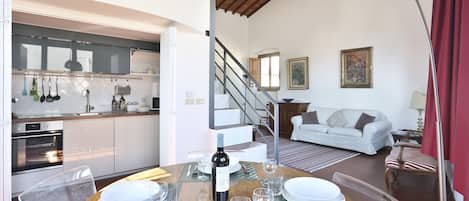 A dining area with a wooden table set for four, a bottle of wine, and a kitchen in the background.