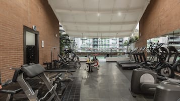 Ein Fitnessraum mit verschiedenen Trainingsgeräten, darunter Laufbändern und Ergometer, und einer Ziegelwand.