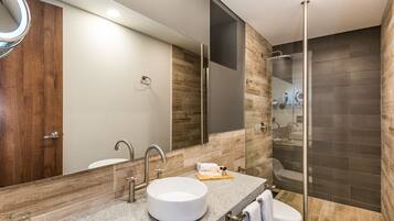 Un baño moderno con un lavabo redondo, un espejo grande, una zona de ducha y un tocador de madera.