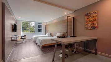Quarto de hotel moderno com duas camas, uma mesa, uma cadeira e uma janela grande com vista para áreas verdes.