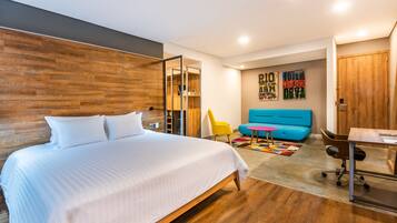 Una habitación de hotel moderna con una cama grande, un sofá azul, una mesita pequeña y una alfombra colorida.
