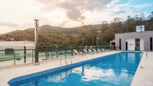 Una piscina con barrera de vidrio, sillas de descanso y vista a un paisaje montañoso.