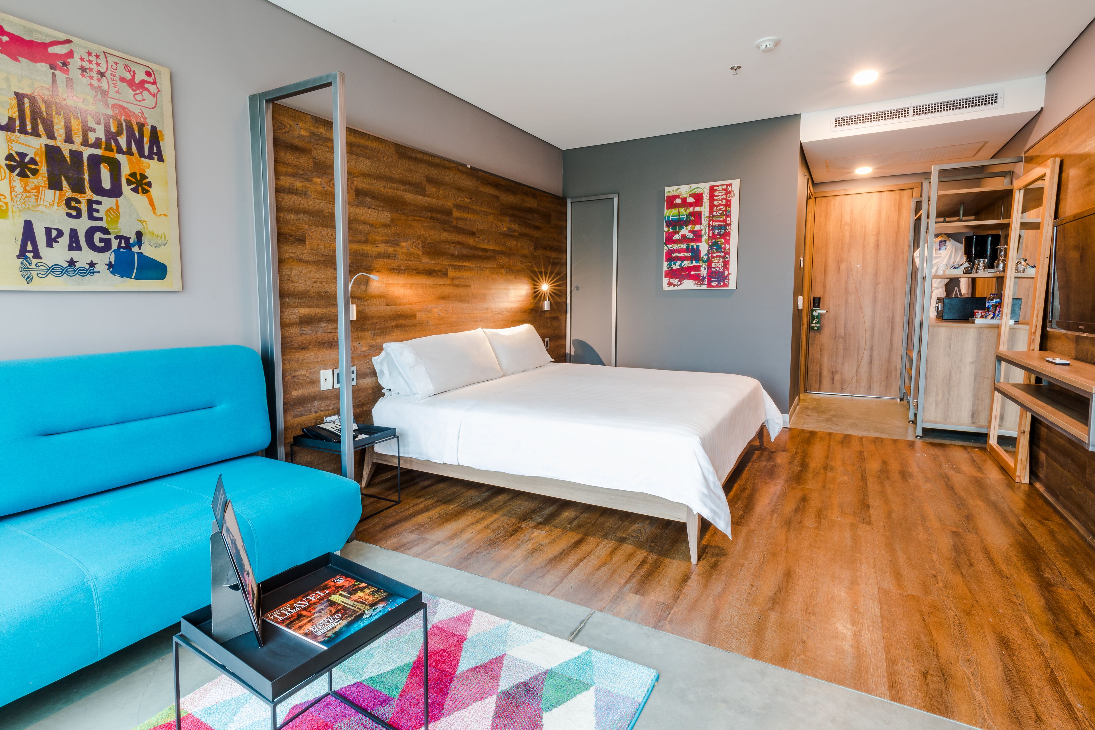Ein modernes Schlafzimmer mit einem Bett, einem blauen Sofa, Holzboden und einem Kleiderschrank.