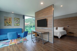 Una habitación de hotel moderna con un escritorio de madera, un televisor de pantalla plana, una cama, un sofá azul y dos sillas azules.