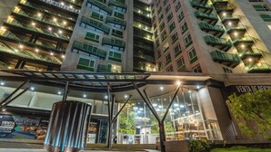 Un edificio de hotel de varios pisos con balcones, fachada de vidrio y una entrada bien iluminada.
