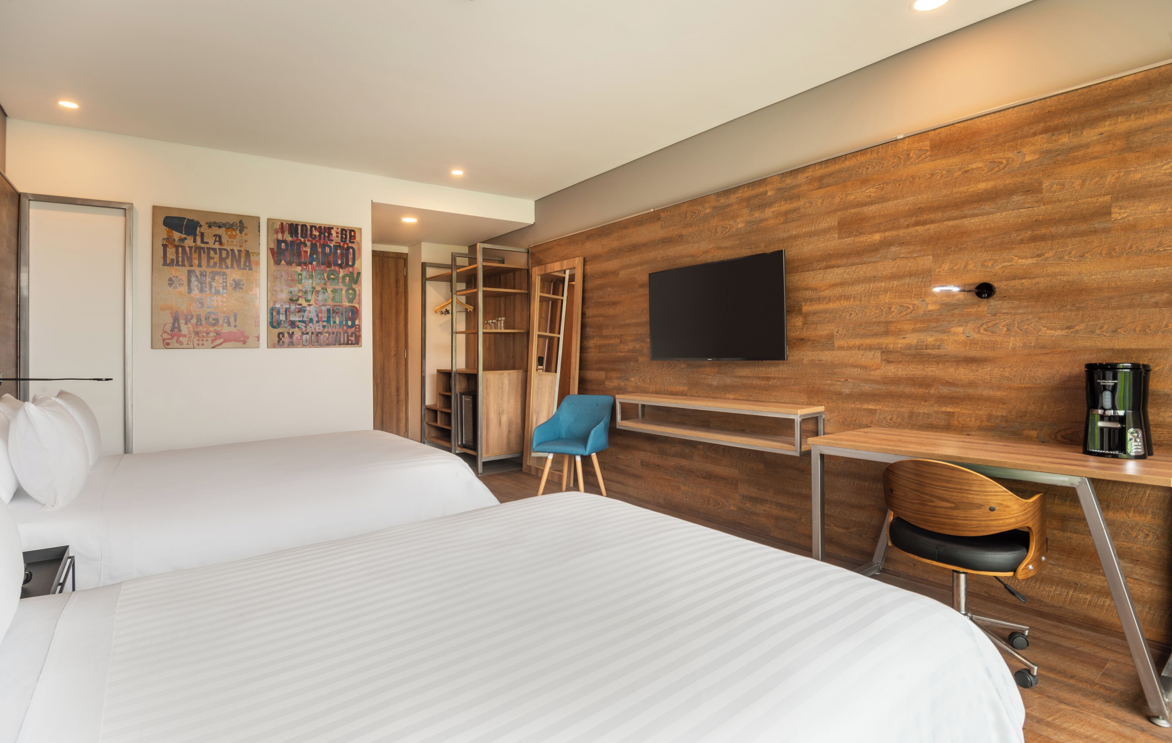 A hotel room with two beds, a desk, a chair, a TV, and a wardrobe.