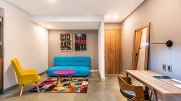 A modern living room with a blue sofa, a yellow chair, a wooden desk, and a colorful rug.
