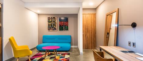 A modern living room with a blue sofa, a yellow chair, a wooden desk, and a colorful rug.