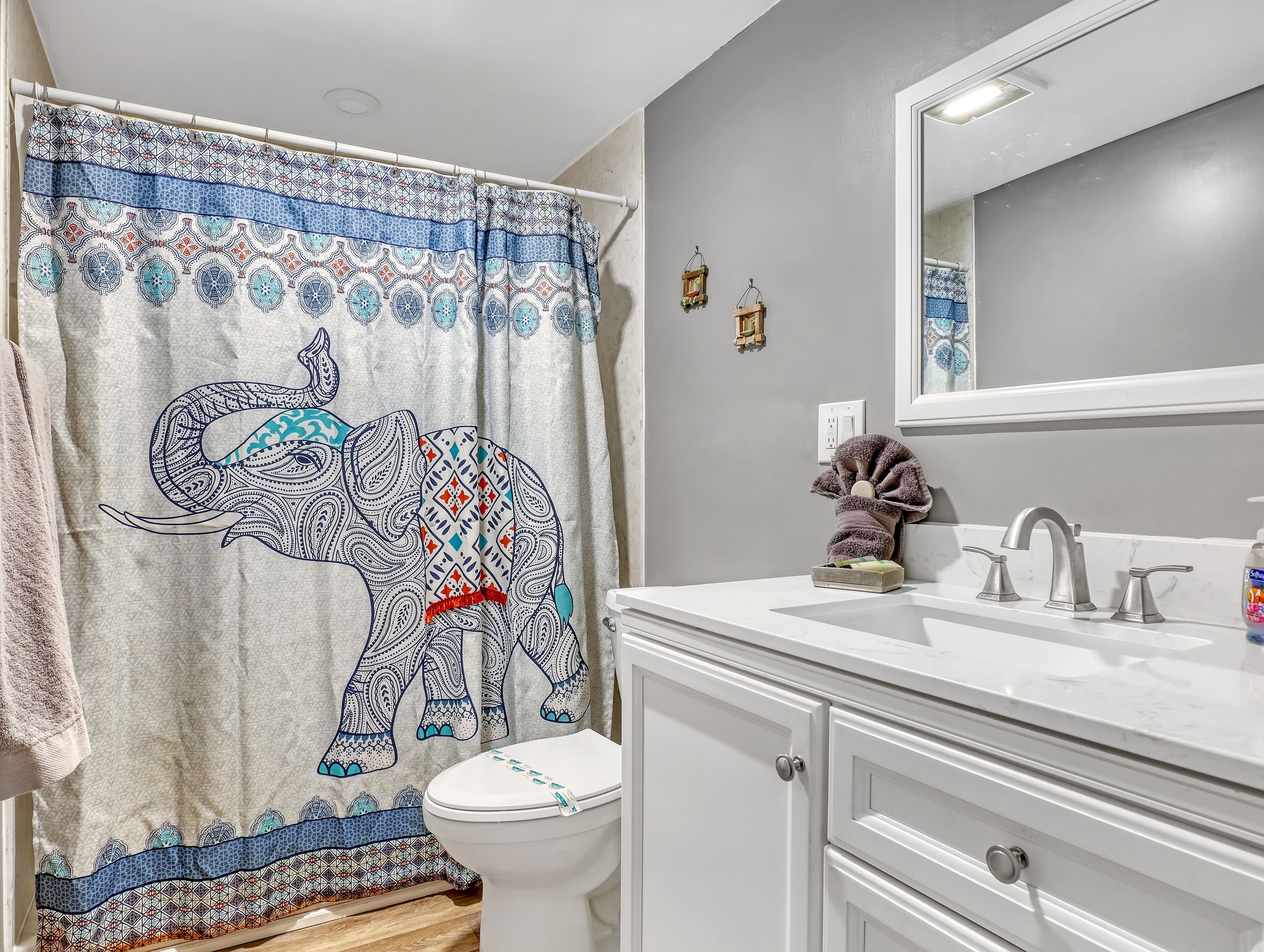 A bathroom with a patterned shower curtain, a toilet, a sink with a mirror, and a towel rack.