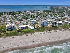 An aerial view of a coastal residential area with beachfront properties, including multi-story buildings and a sandy beach.