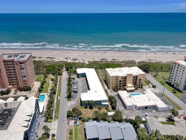 A beachfront hotel with multiple buildings, a parking lot, and a view of the ocean.