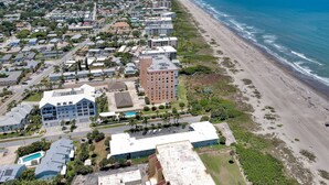 An aerial view of a coastal town with a beachfront, residential buildings, and a large hotel with a swimming pool. - RIGHT ON THE BEACH!!  Rockets and Cruise Ships! Kid and pet friendly, 2Br.   (Cocoa Beach)