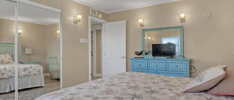 A bedroom with a large bed, a dresser with a TV, a mirror, and a closet.