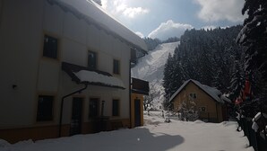 Un edificio cubierto de nieve con techo inclinado, un pequeño porche y un camino que lleva a una montaña.