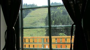 Una ventana con vista a una terraza de madera y una colina cubierta de césped.