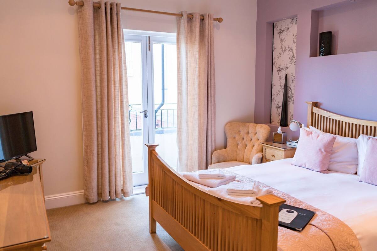 A hotel room with a wooden bed, a chair, a TV, and a balcony with curtains.
