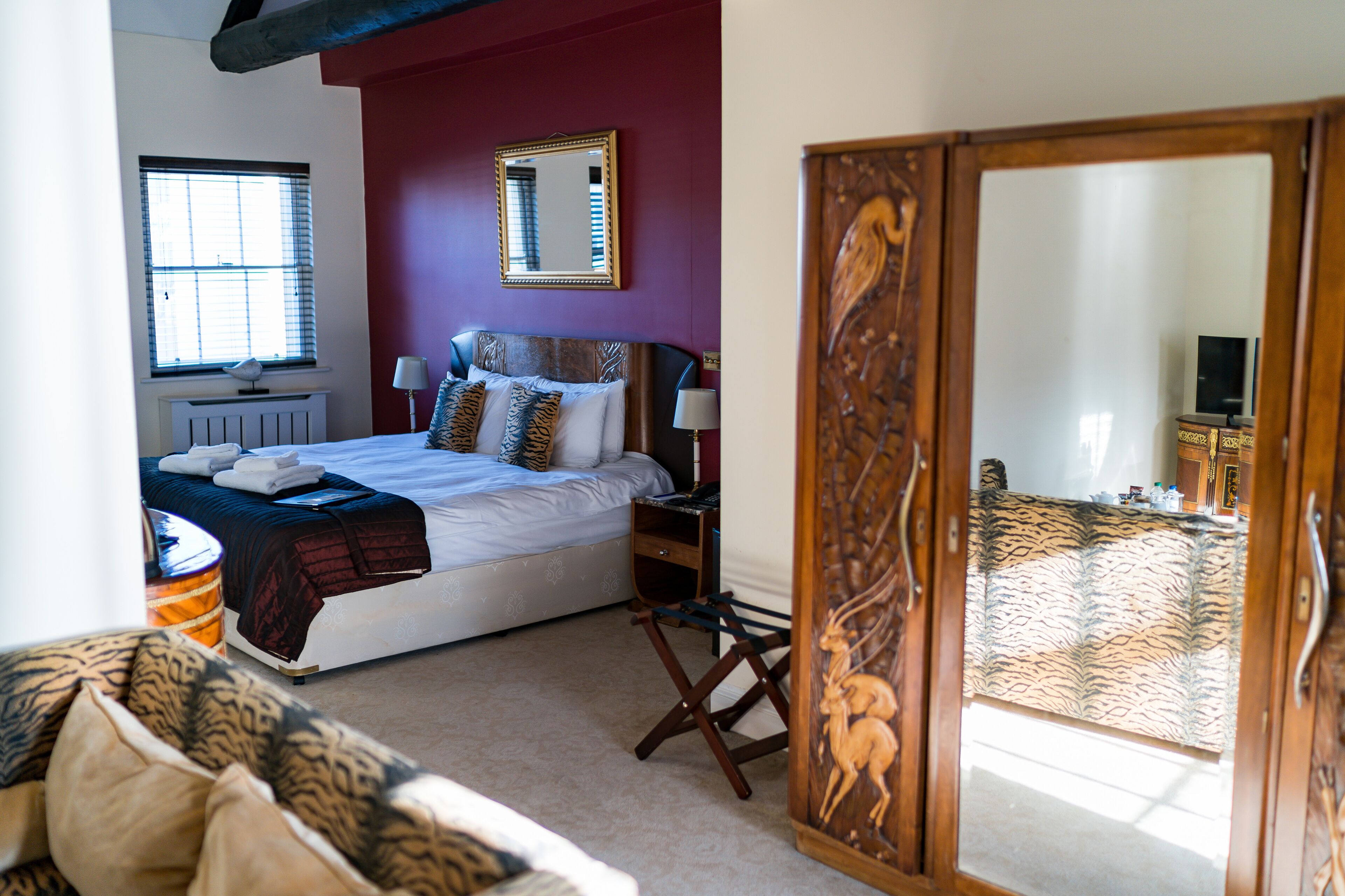 A bedroom with a bed, bedside table, lamp, window, radiator, and a wardrobe with a mirror.