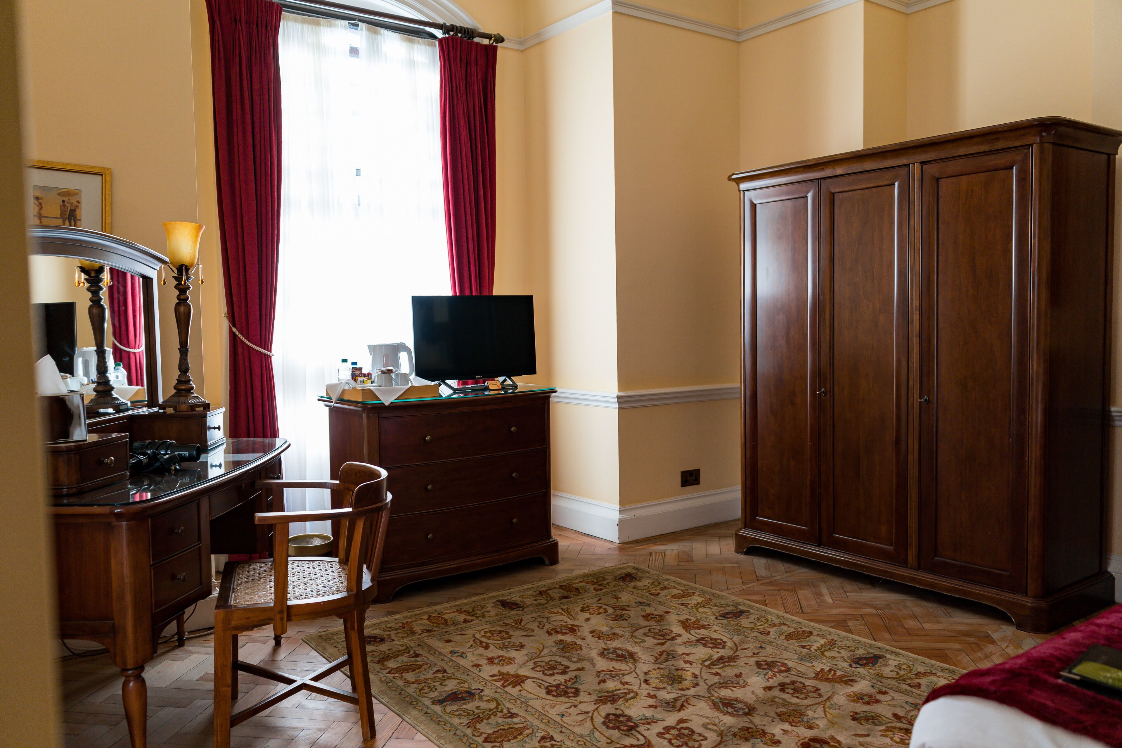 Une chambre d’hôtel avec un bureau en bois, une télévision, une armoire et un tapis à motifs.