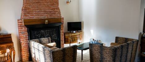 Una sala de estar con chimenea de ladrillo, televisor y muebles con diseños.