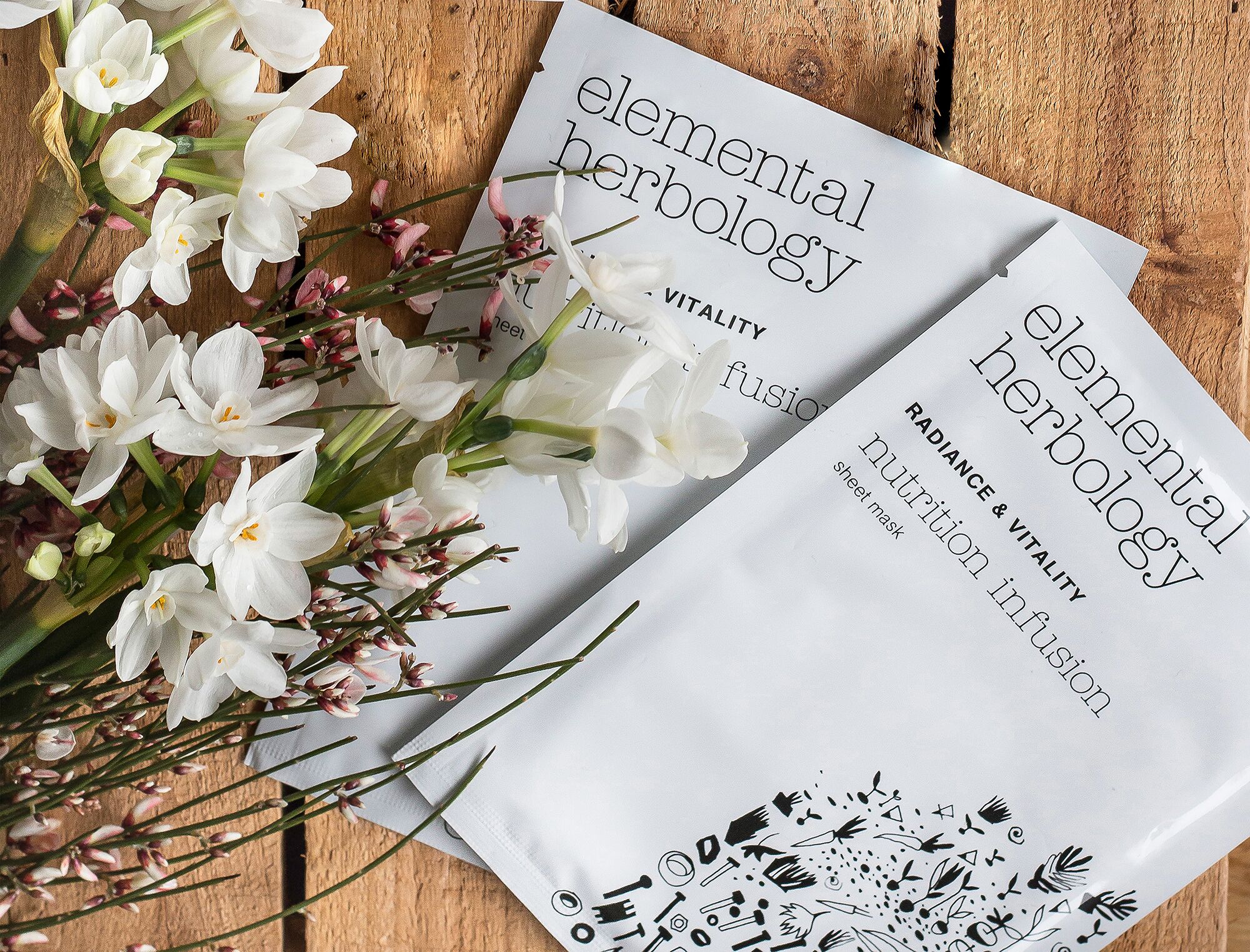 A wooden surface with a white paper titled "elemental herbalology" and a bouquet of white flowers.