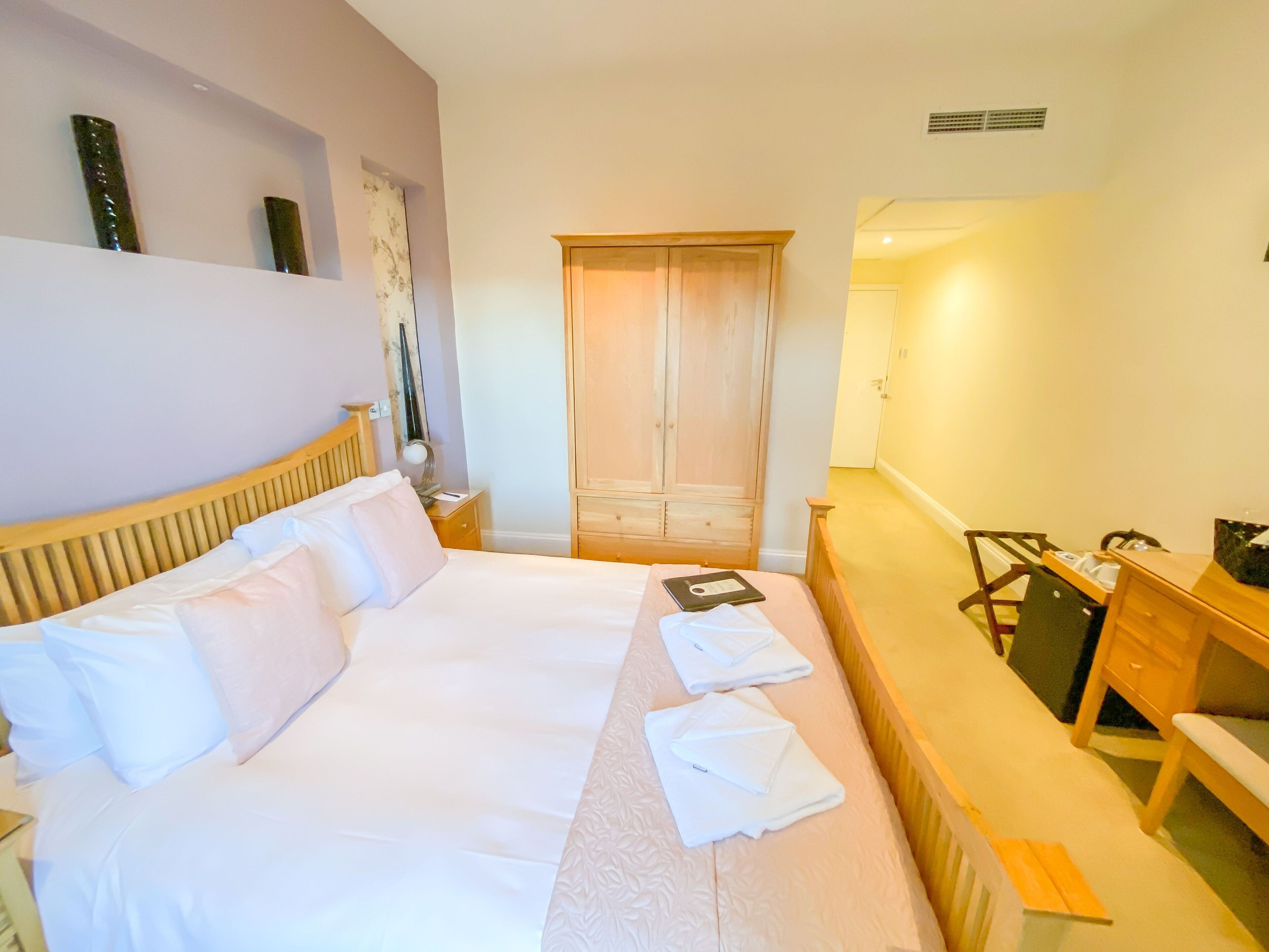Une chambre d’hôtel avec un grand lit, un bureau en bois, une chaise, une armoire et une table de chevet avec une lampe.
