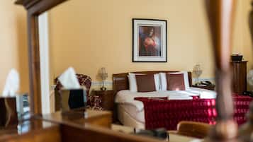 A hotel room with a large bed, a bedside table with a lamp, a framed picture on the wall, and a mirror reflecting part of the room.