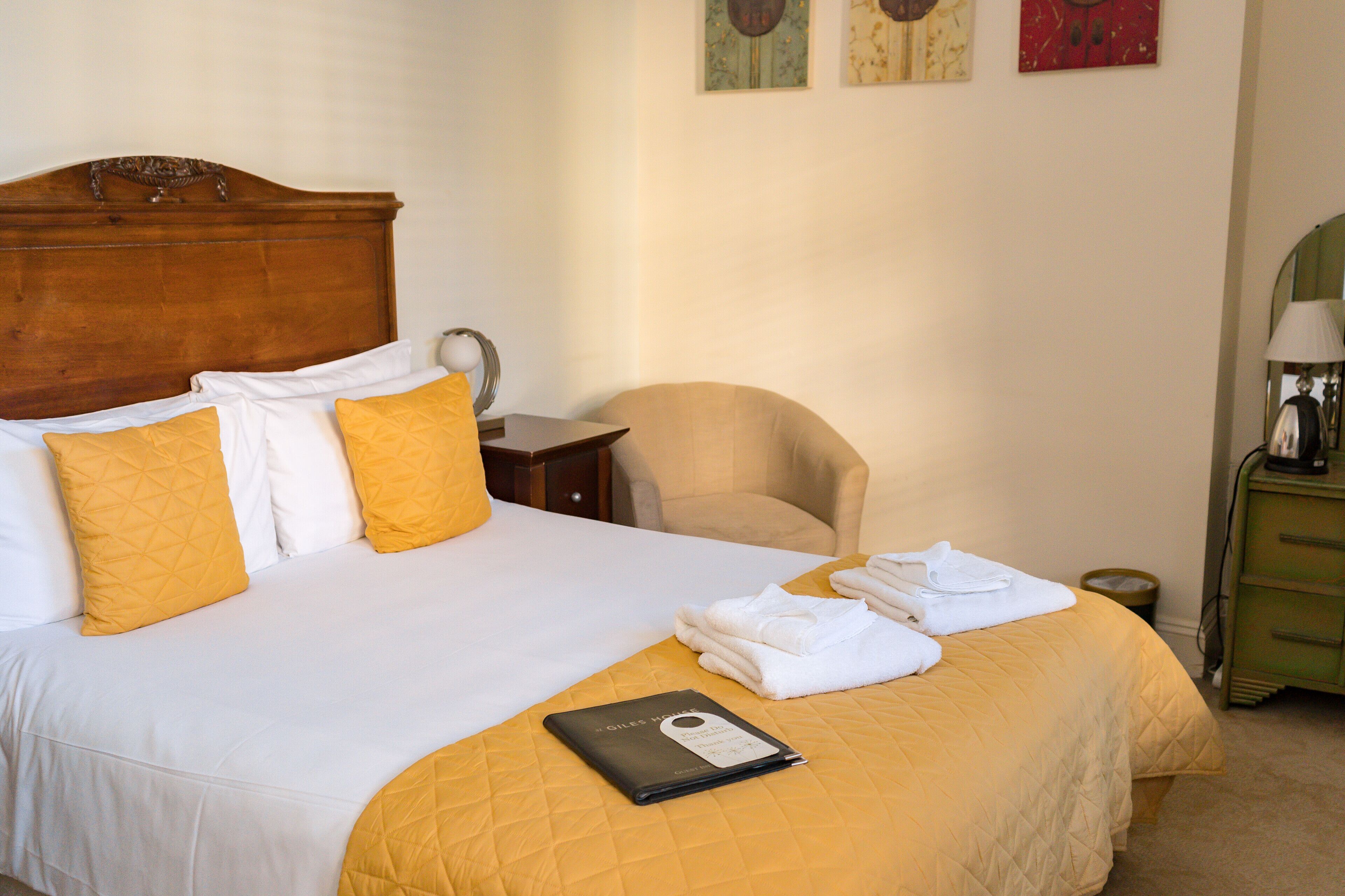 A neatly made bed with a wooden headboard, a bedside table with a lamp, and a chair.
