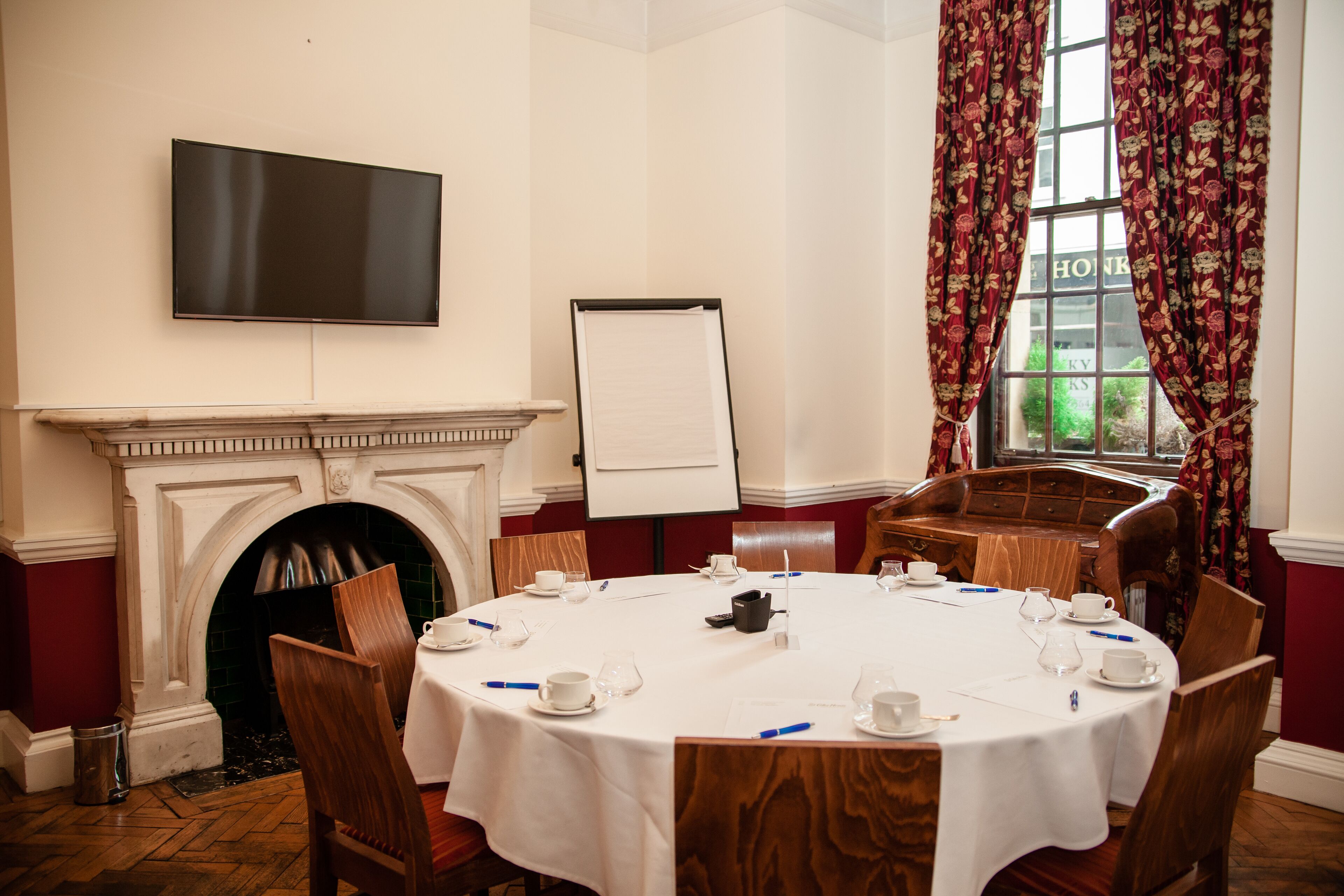 A conference room with a round table, chairs, a fireplace, a whiteboard, and a television.