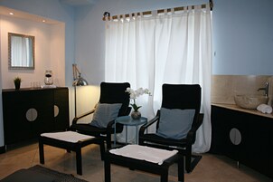 Ein Zimmer mit zwei schwarzen Stühlen, einem kleinen Tisch mit einer Lampe, einem Spiegel und einem weißen Vorhang.