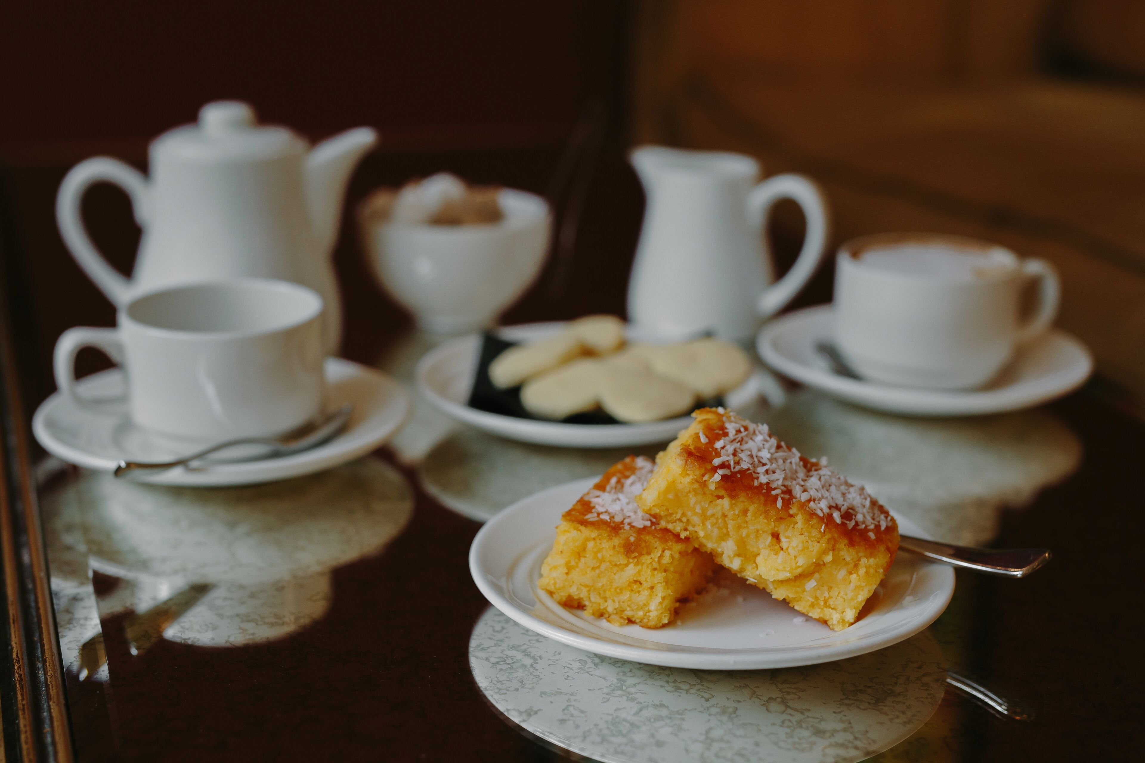 A table with a plate of cake, a teapot, cups, and a bowl of cookies.