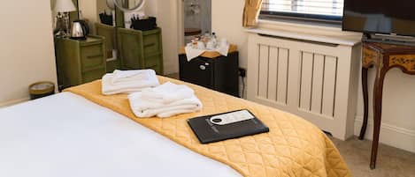 A hotel room with a bed, a bedside table with a lamp, a dresser with a mirror, a radiator, and a television.