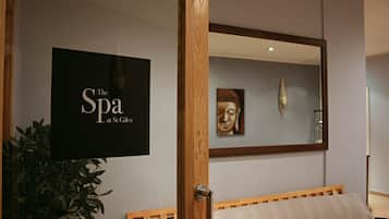 Una habitación con una cama, un cartel en la pared que dice "The Spa at St Giles", un espejo que refleja una estatua de Buda y una planta en maceta.