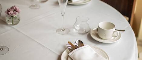 A neatly set dining table with white tablecloth, plates, cutlery, and a glass of water.