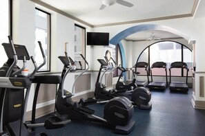Sala de ginástica com esteiras, elípticos e uma televisão.