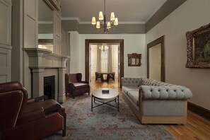 A living room with a fireplace, leather chairs, a sofa, a coffee table, and a chandelier. - The Driskill (Austin)