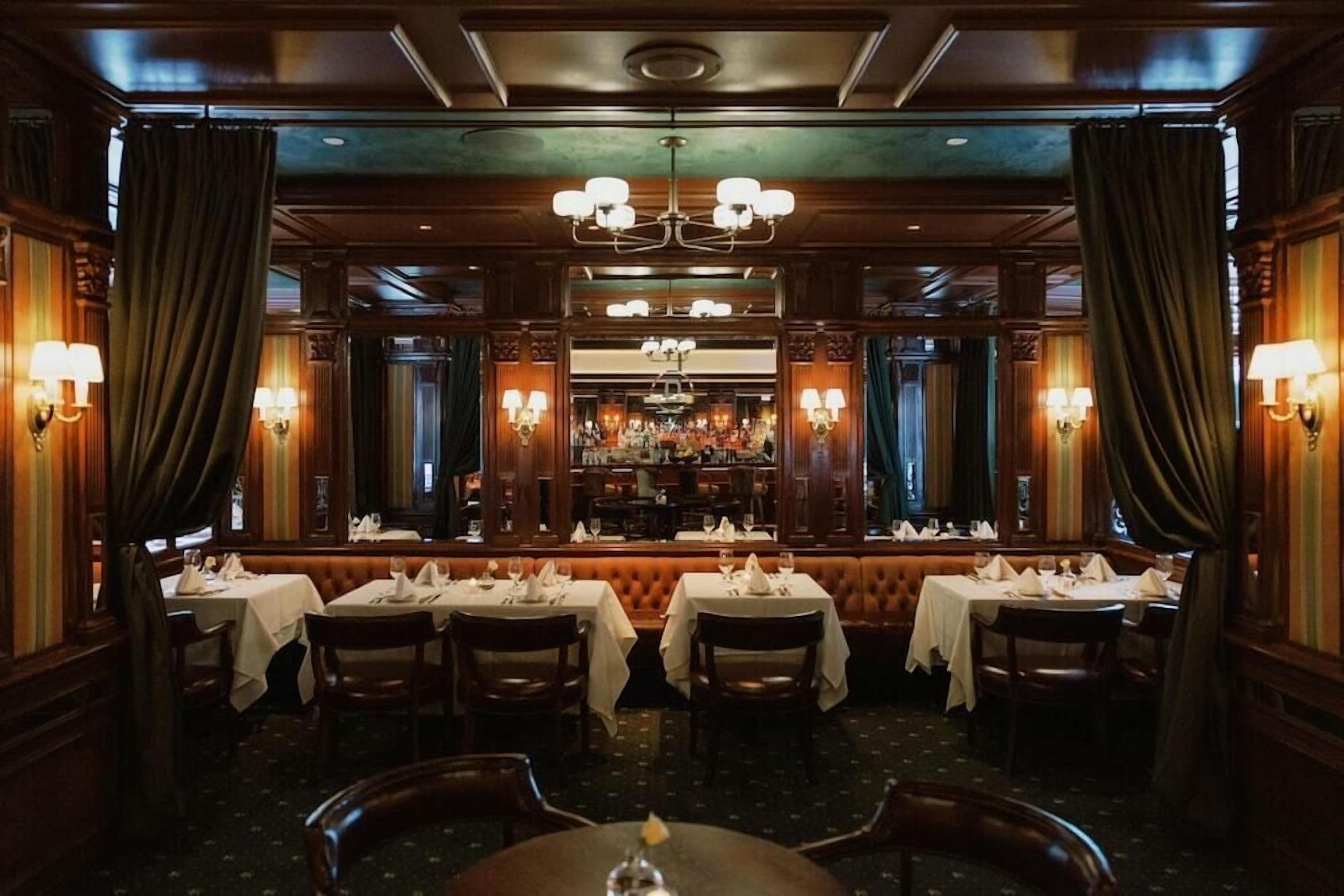 A restaurant with multiple tables, chandeliers, and wall sconces.
