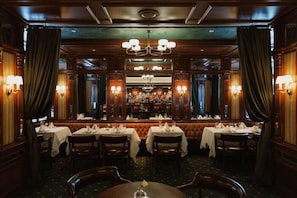A restaurant with multiple tables, chandeliers, and wall sconces. - The Driskill (Austin)