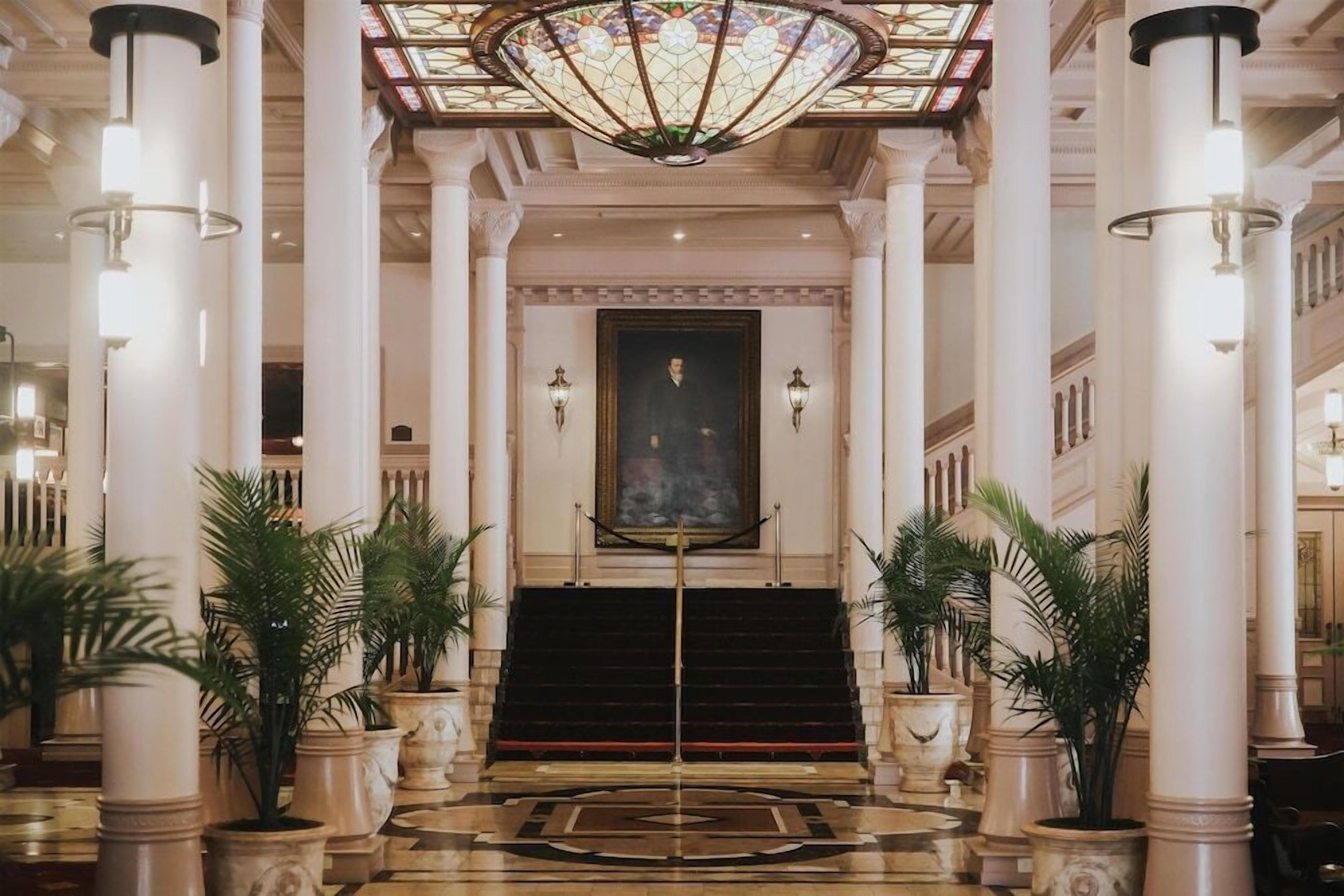 A grand lobby with a central staircase, large columns, and a stained glass ceiling.