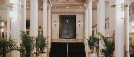 A grand lobby with a central staircase, large columns, and a stained glass ceiling.