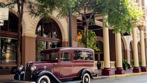 Une voiture ancienne est garée devant un bâtiment historique doté d’arcades et de colonnes.