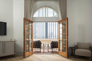 A room with a large arched window, a wooden door with glass panels, a small table with two chairs, and a sofa. - The Driskill (Austin)