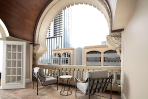 A balcony with two chairs and a small table, overlooking a cityscape with modern buildings. - The Driskill (Austin)