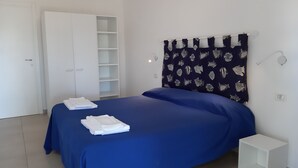 A bedroom with a bed, a wardrobe, a bedside table, and a curtain with a fish pattern. - Hotel Grotte del Paradiso (Portoferraio)
