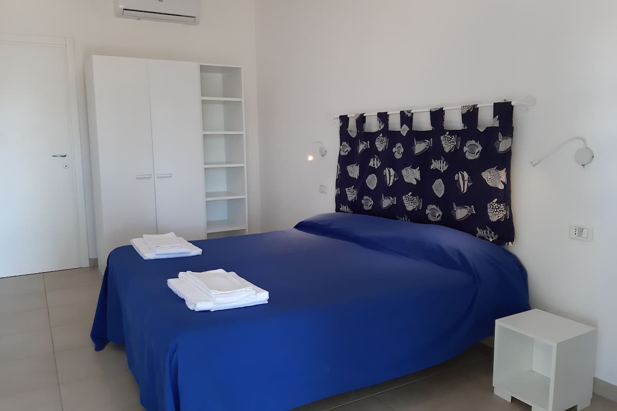 Un dormitorio con cama, armario, mesita de noche y cortina con estampado de peces.